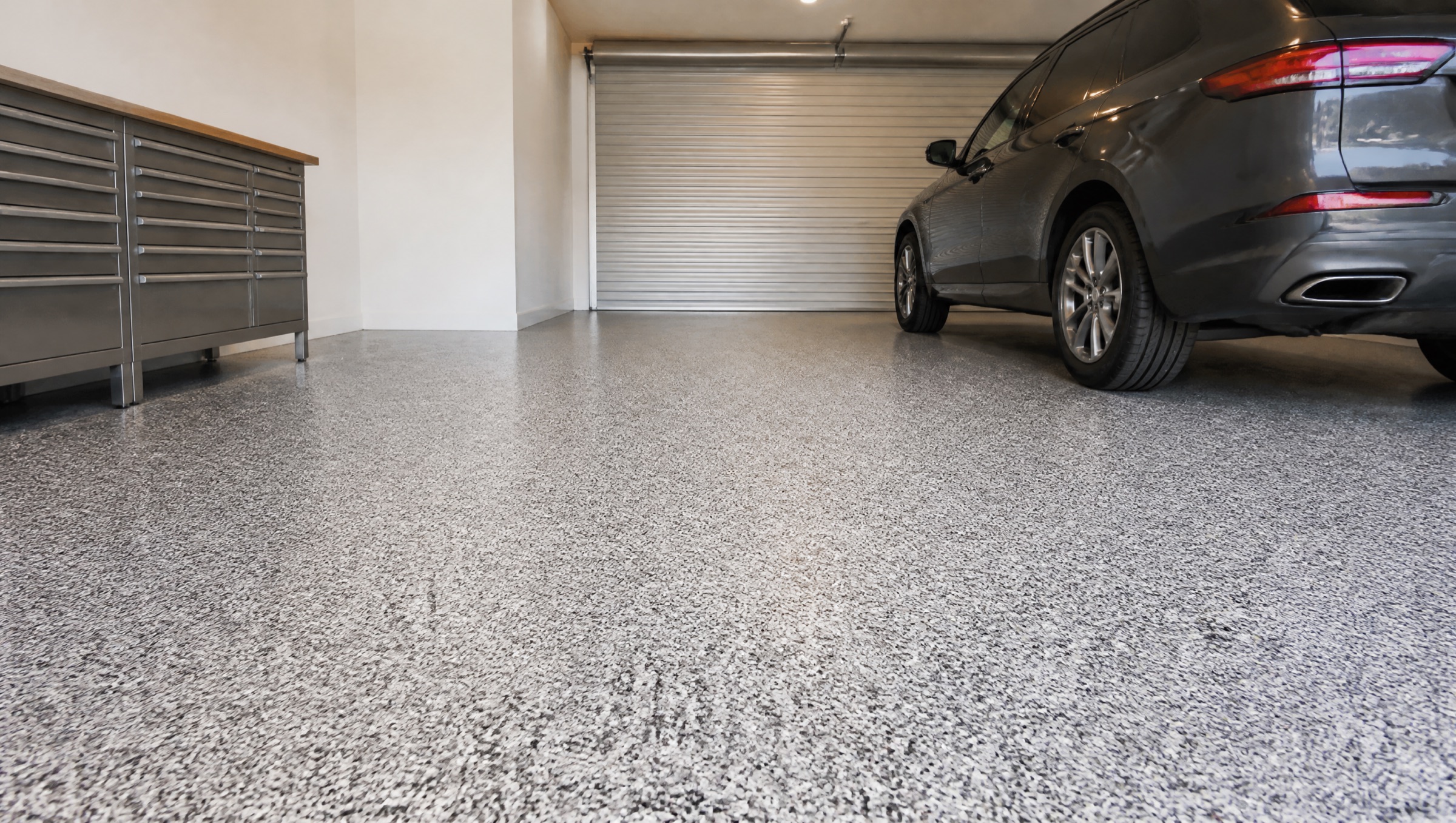 A home garage with a grey, white and charcoal flake floor and a dark SUV parked on it