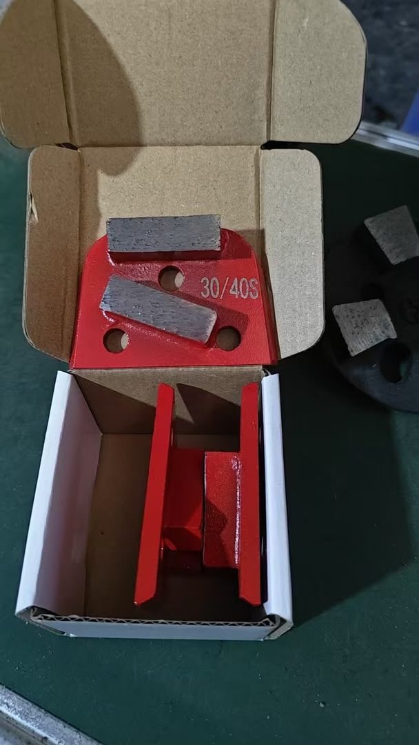 A red trapezoid grinding shoe stamped 30/40S, two diamond segments brazed to its face, lying in its box