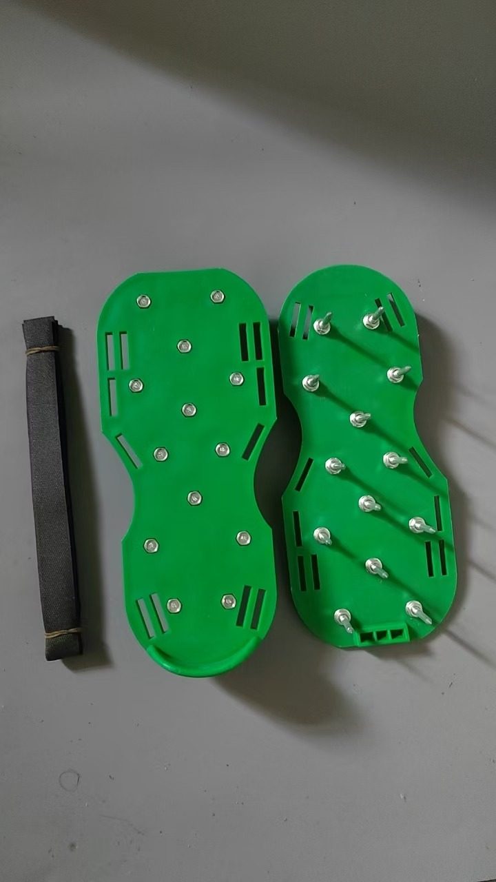 A pair of green plastic spike shoes with steel spikes and a strap, on a floor
